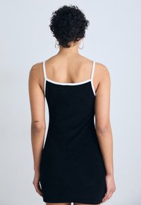 Vestido negro sin mangas con una silueta ajustada, ribete blanco en el escote y las sisas, confeccionado con una tela suave y texturizada.