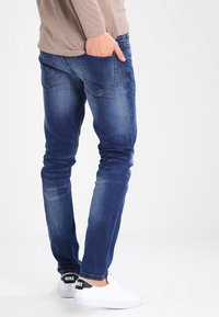 Mörkblå denimjeans med slim fit, med bakfickor och subtil blekning; bärs tillsammans med vita sneakers med svarta accenter.