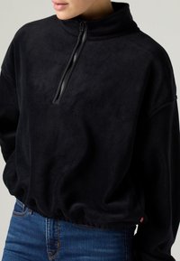 Μαύρο φλις πουλόβερ με γιακά μισού φερμουάρ, χαλαρή εφαρμογή και ελαστικό τελείωμα. Διαθέτει ομαλή υφή και μινιμαλιστικό σχεδιασμό.