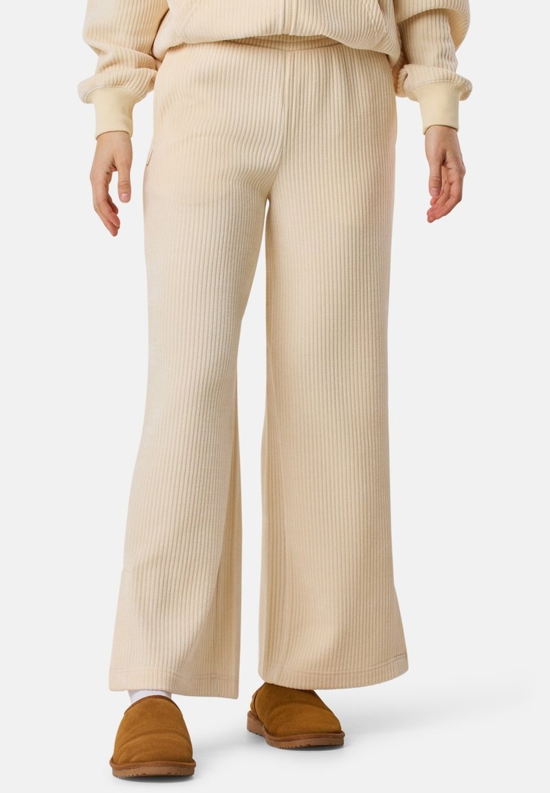 Beige geribbelde flared pants met een zachte textuur, voorzien van een elastische tailleband. Gedragen met bruine instappers.