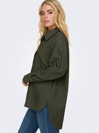Camisa de corduroy verde-oliva com colarinho botão, mangas longas e fendas laterais para maior liberdade de movimento. O tecido texturizado apresenta riscas verticais.