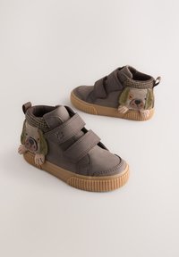 Braune High-Top-Schuhe mit zwei Klettverschlüssen, Gummisohlen und einem hundeartigen Akzent an der Seite mit strukturierten Details und Farben.