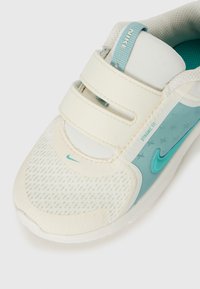 Chaussure de sport blanche avec des accents turquoise, dotée d'une tige en mesh, de deux bandes Velcro et d'une semelle texturée pour l'adhérence et le confort.