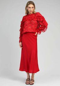 Blouse en dentelle rouge avec des manches volantes, associée à une jupe en satin rouge. La jupe est lisse et fluide, tandis que la blouse présente des motifs floraux.