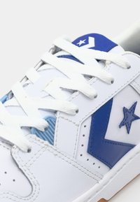 Hvit sneakers med blå detaljer og stjernemønster. Laget av lær med teksturerte pålegg og hvite snører, gummisåle.