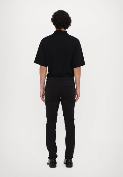 Svart kortärmad polo t-shirt i kombination med svarta slim-fit byxor och svarta skor, sedd bakifrån, som visar upp en minimalistisk design.