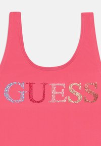 Rožinė maikutė su užrašu "GUESS" spalvingais deimantais, su lygia tekstūra ir suapvalintu kaklu.