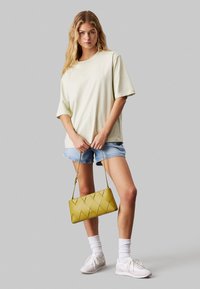 Camiseta oversized verde claro, shorts de denim, zapatillas blancas y un bolso amarillo con patrón de diamante acolchado. Tejido suave y estilo casual.