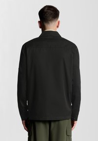 Sort langærmet skjorte med krave, knapmanchetter og lige kant. Glat tekstur, minimal branding og detajler på bagstykket.