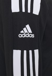 Svart idrettsplagg med hvit tre-stripes design og adidas-logo på siden. Laget av teksturert stoff.