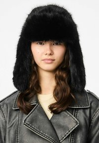 Czarna czapka trapper z sztucznego futra z klapkami na uszy, o miękkiej, puszystej fakturze i zaokrąglonym wierzchu, noszona przez modelkę z długimi, falującymi włosami.