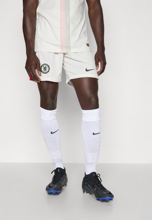Maglietta da calcio bianca Nike con strisce verticali colorate, pantaloni corti bianchi con logo Chelsea, scarpe da calcio nere e blu e calze bianche con logo Nike.