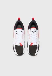 White sneakers with black mesh panels, red accents, and textured soles. Features lace-up design and heel pull tab.