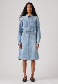 Ανοιχτό μπλε πουκάμισο τζιν με κουμπιά και δύο τσέπες στο στήθος, σε συνδυασμό με φούστα τζιν μήκους μέχρι το γόνατο, στο ίδιο χρώμα. Ομαλή υφή, κλασικός σχεδιασμός.