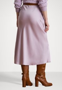 Lavendel sateng midi skjørt med en glatt tekstur, som har en svak glans. Kombinert med brune lærhelsestøvler med spennedetalj.