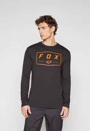 T-shirt noir à manches longues en coton, arborant un logo rectangulaire orange avec "FOX" et une icône, avec un col rond et une coupe ajustée.