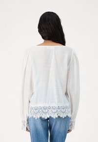 Witte blouse met lange, geplofte mouwen en kanten details bij de manchetten en onderkant. Zachte, lichte stof, geschikt voor casual wear.