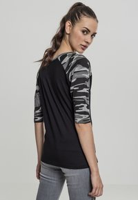Maglietta nera con maniche a 3/4 in camouflage grigio. Presenta un design aderente e una texture morbida, evidenziando un aspetto sportivo ma casual.