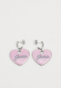 Orecchini a forma di cuore in smalto lucido rosa, con il logo "Guess" in grigio, dotati di hardware in metallo argentato e chiusura a gancio.