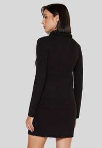 Abito nero a maniche lunghe con un motivo strutturato, forma aderente e un dettaglio con collana di perline sullo scollo.