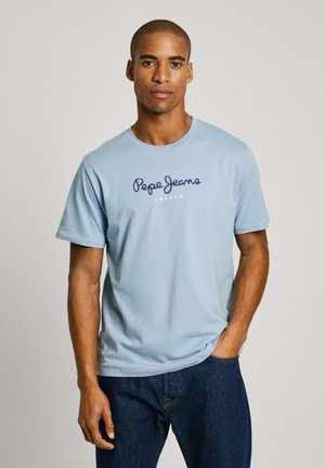 Svijetloplava pamučna majica s okruglim izrezom, na kojoj je tamnoplavi logo "Pepe Jeans London" preko prsa. Kratki rukavi, ležeran kroj.