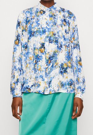 Langærmet bluse med knapper, med blåt, gult og hvidt blomsterprint, båret med et teal-farvet skørt, vist fra nakke til hofter.