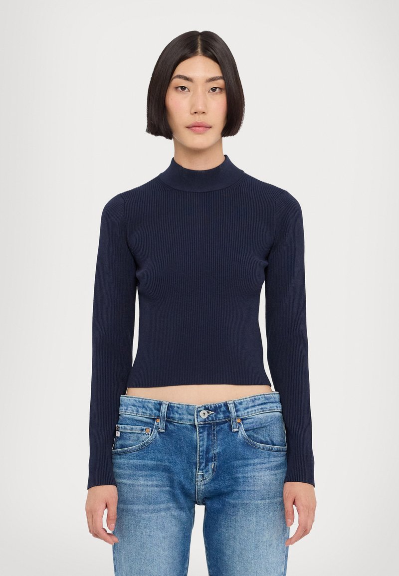 Pull en maille côtelée navy à col roulé, avec des manches longues, associé à un jean bleu clair déchiré avec fermeture à bouton et poches avant.