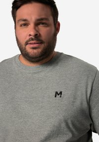 Šedá bavlněná mikina s kulatým výstřihem, která má na hrudi malé černé logo "M", texturovanou látku a klasický střih.