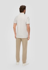 Helles beiges Polo-Shirt mit kurzen Ärmeln und Kragen, kombiniert mit beigen Hosen. Der Stoff wirkt weich, mit einer lockeren Passform und glatter Textur.