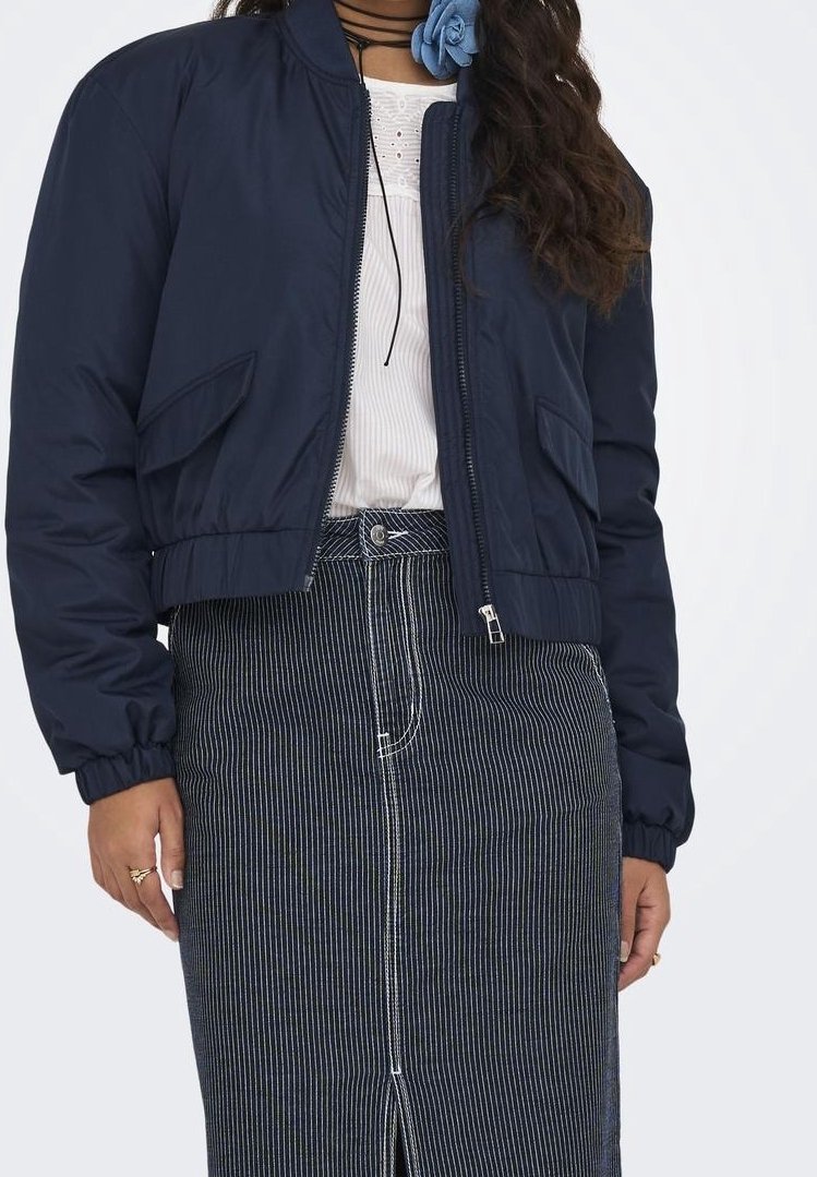 Femme portant une veste bomber bleu marine sur un chemisier blanc et une jupe taille haute rayée avec une fente à l'avant.