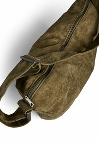 Olive krāsas zamšādas soma ar teksturētu virsmu, ar rāvējslēdzēju un auduma siksnu. Iezīmē metāla akcentu tuvumā rāvējslēdzējam, lai nodrošinātu izturību.
