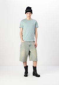 Μιντ πράσινο κοντομάνικο T-shirt, oversized ξεθωριασμένα τζιν σορτς και μαύρες δερμάτινες μπότες μέχρι τον αστράγαλο. Μαύρη σκούφος με λευκό κείμενο.