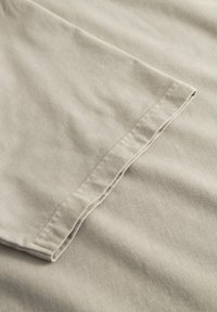 Lysegråt bomuldsstof med en blød tekstur, der viser en glat overflade og kantdetalje med rullet søm.