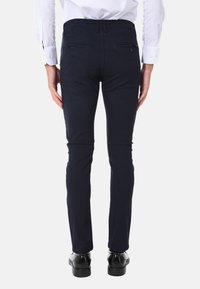 Pantaloni su misura blu navy con una texture liscia, vestibilità slim e due tasche posteriori. Indossati con una camicia bianca e scarpe nere.