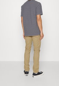 T-shirt a righe navy e bianche, pantaloni beige, sneakers nere. Look casual con maniche corte e collo rotondo su uno sfondo neutro.