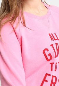 Felpa rosa con testo ricamato rosso "TUTTE LE RAGAZZE A FR." Presenta un collo tondo e un tessuto testurizzato. Cuciture visibili e vestibilità comoda.