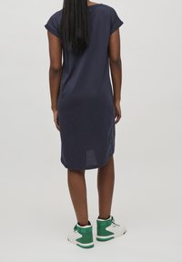 Robe bleu marine mi-longue avec des manches courtes retroussées, fabriquée en tissu doux ; associée à des baskets blanches et vertes.