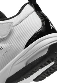 Witte en zwarte sportieve schoen met een gladleren bovenwerk, gestructureerde grijze accenten en een rubberen buitenzool met een patroon voor grip.