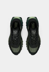 Sneaker nere e verde scuro con suola robusta, realizzate in materiali sintetici e mesh, punta rinforzata e cuciture decorative.