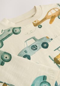 Jasnobeżowa bluza z nadrukiem zabytkowych samochodów i samolotów w kolorach morskim, musztardowym i ciemnozielonym. Żebrowany dekolt i miękka tekstura.