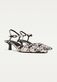 Pointed-toe slingback shoes with a black and white spotted pattern, featuring a slim ankle strap and a low kitten heel.