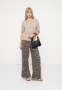Μπεζ πλεκτό πουλόβερ, φαρδιά παντελόνια με λιονταρόκεντρα και μία μικρή μαύρη τσάντα με τρουκς. Μοντέλο που φορά μπεζ πλατφόρμες.