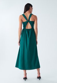 Sügavrohelisest kangast maxi kleit, millel on laiad õlapaelad, keerutatud seljatagune disain ja seljal avatud lõikega detail.