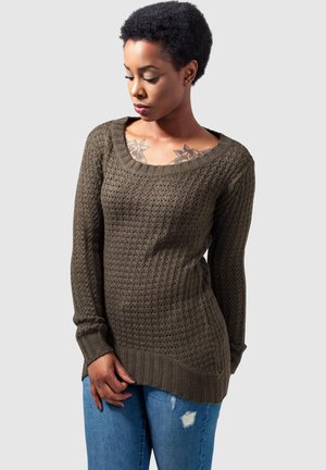 Pull en tricot vert olive avec un motif texturé, encolure large et ronde, et manches longues. Associé à un jean déchiré bleu clair.