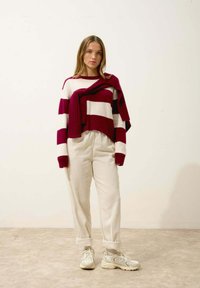 Pull en tricot rayé rouge et blanc, coupe ample, superposé à un pantalon beige texturé et des baskets blanches avec des accents subtils.