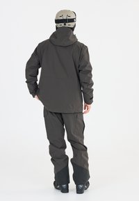 Hiihtopuku tummanharmaasta materiaalista, johon kuuluu pitkä huppujacketti ja cargo-housut mustilla yksityiskohdilla. Mukana tulee kypärä säädettävillä hihnoilla.