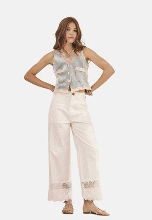 Chaleco corto de textura y con botones en patrón blanco y negro; pantalones anchos beige con adornos de encaje en el dobladillo; combinado con sandalias planas.