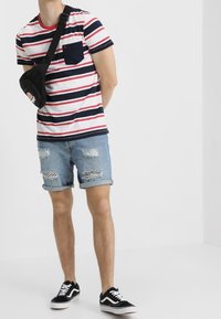 Pruhované tričko s krátkým rukávem v bílé, červené a námořnické modři; džíny šortky s roztrhanými detaily; černé tenisky; malá crossbody kabelka.