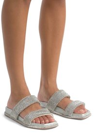Infradito argentate glitterate con due larghe cinghie, decorate con strass e una base morbida grigia. Suola piatta, design open-toe.