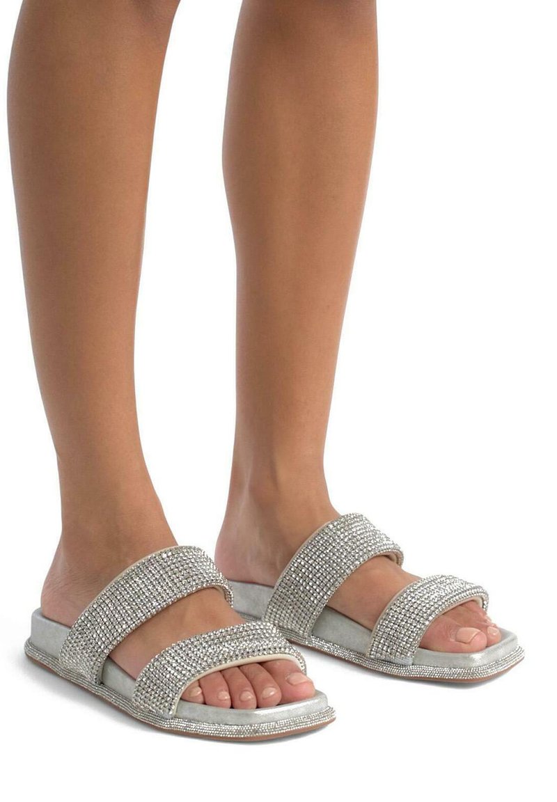 Silberne Glitzer-Sandalen mit zwei breiten Riemen, verziert mit Strasssteinen und einem sanften grauen Grundton. Flacher Absatz, offene Zehenpartie.